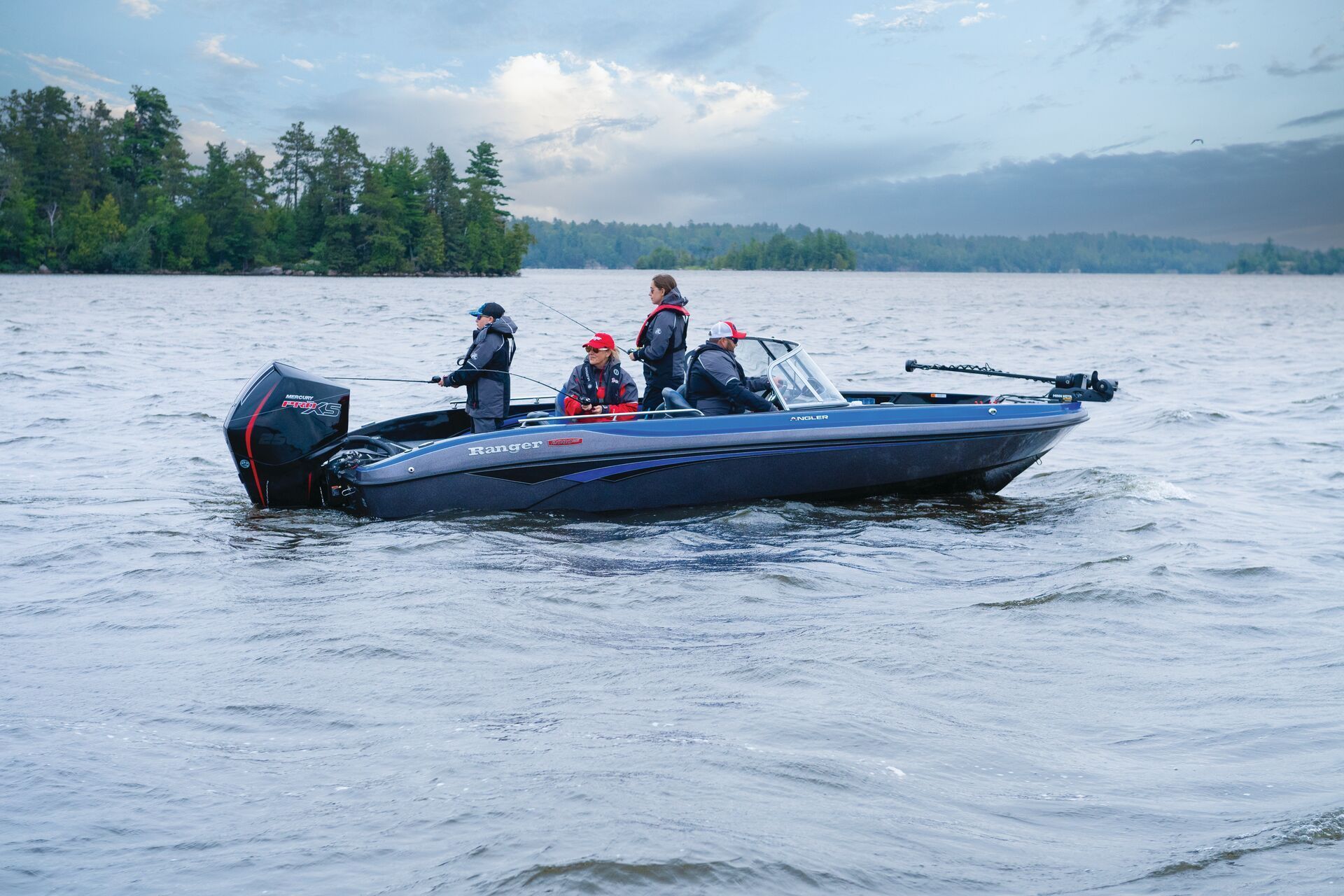 A red motorboat on a lake at sunset with two people onboard, while a third person swims nearby with a wakeboard.