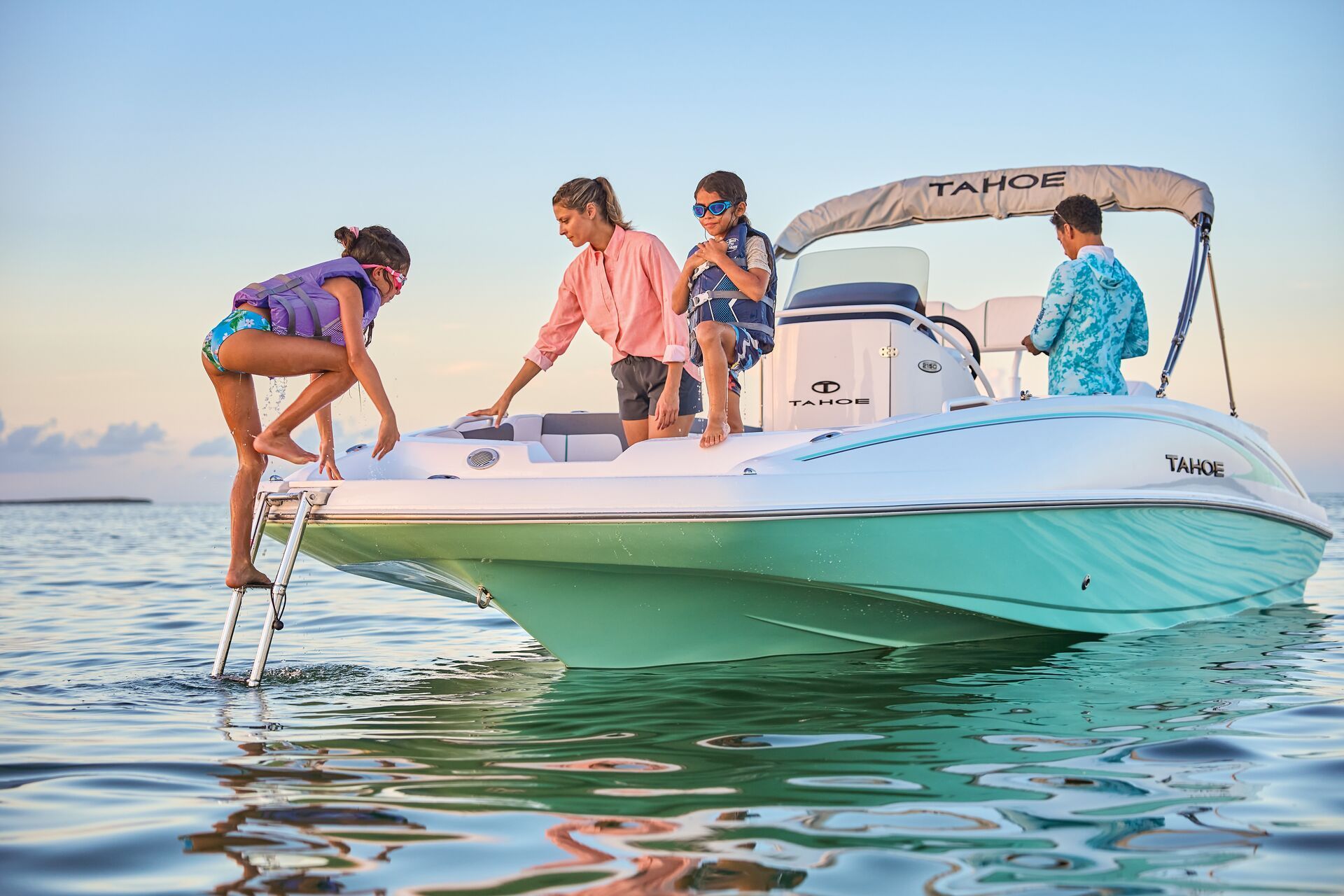 A family boards a bright turquoise Tahoe boat from a ladder in calm water at sunset.