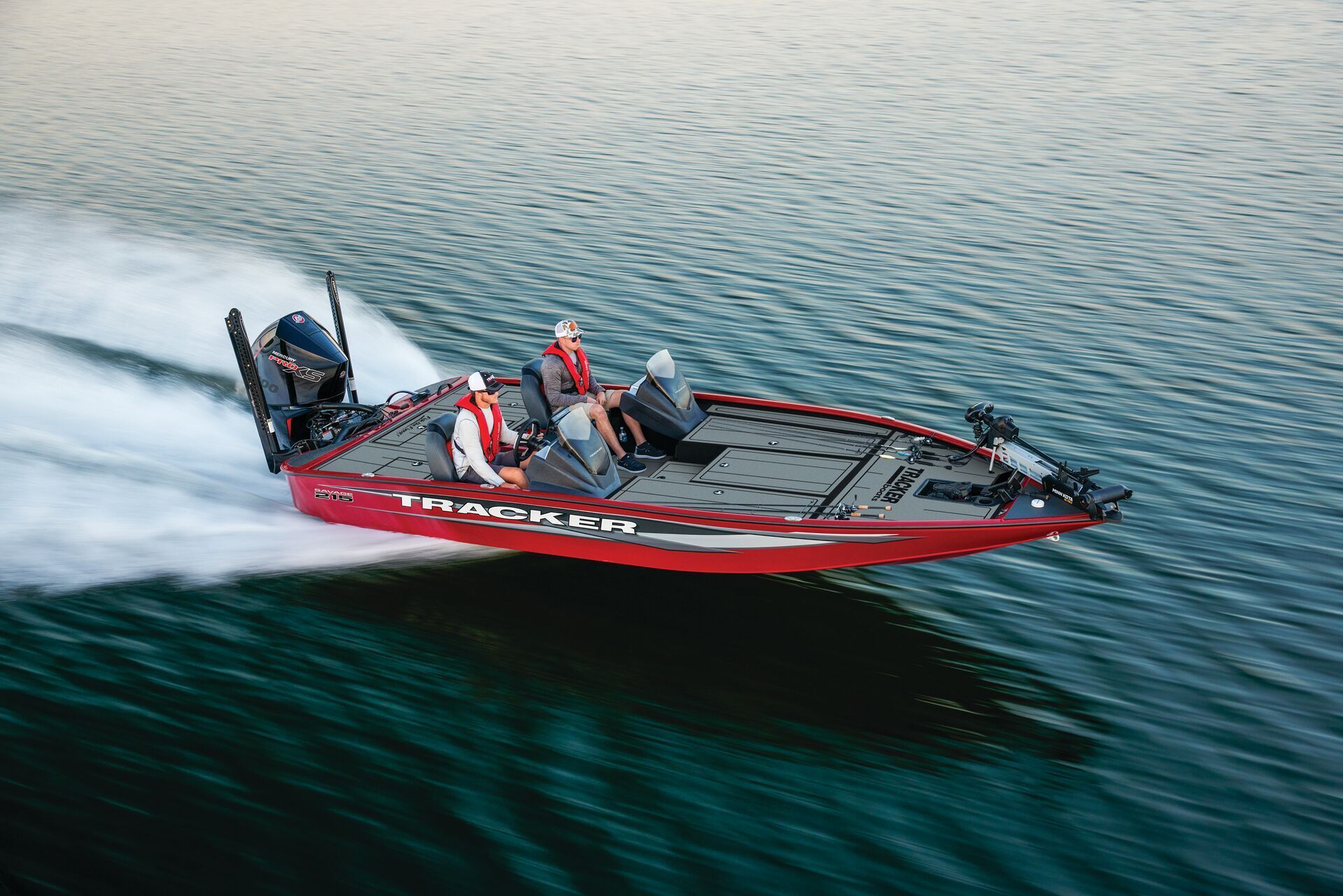 A red bass boat with two people speeding across calm water, leaving a white wake.