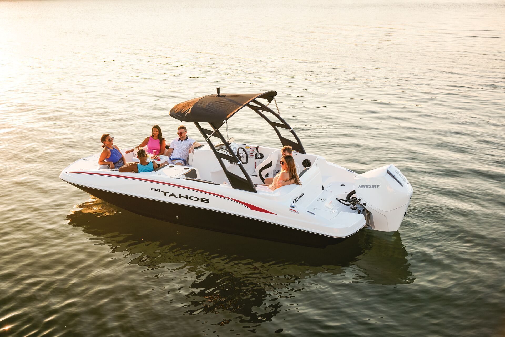 A white TAHOE motorboat with a black canopy carries five people on calm, sunlit water.