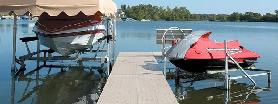 A dock with a covered boat and a red jet ski in the water. Trees are in the background.