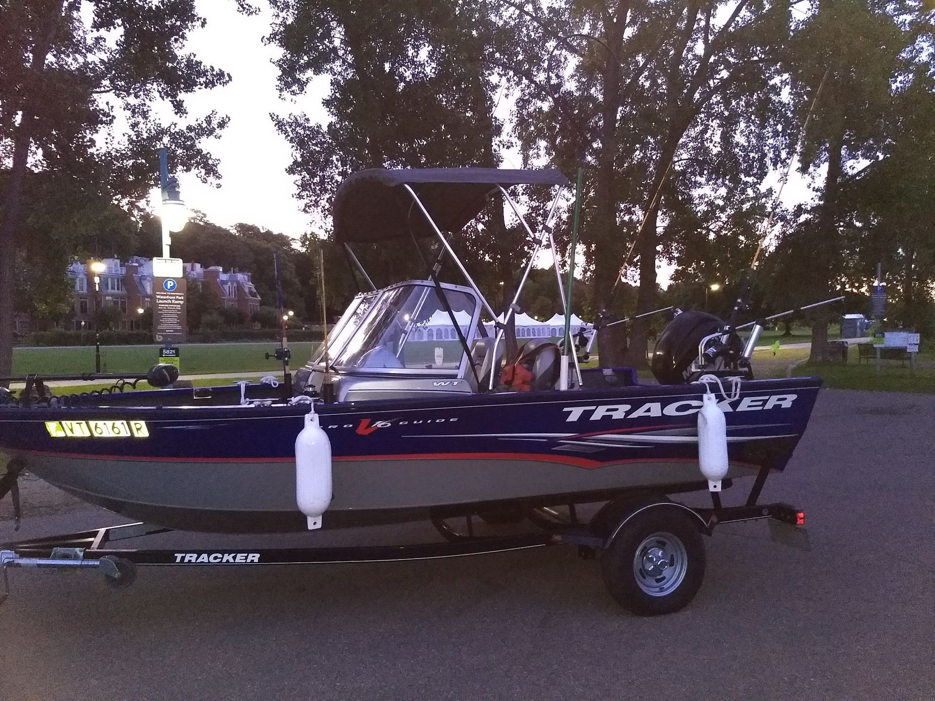 Blue and gray Tracker fishing boat on a trailer, with fishing rods, canopy, and two white buoys.