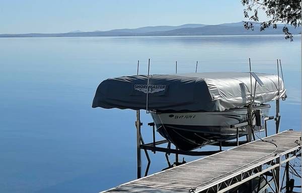 Boat docked on a lift with a cover, overlooking a calm lake and distant mountains.