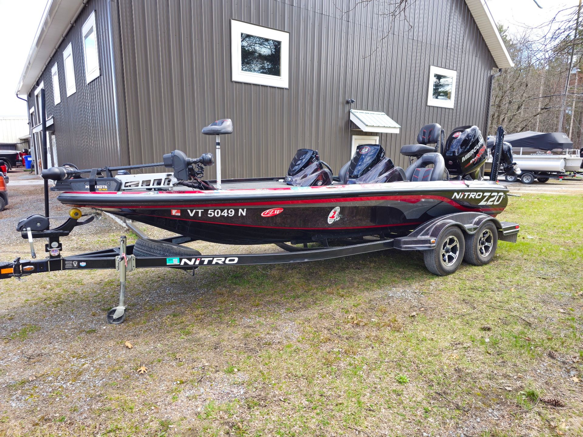 Black and red Nitro bass boat on a trailer, parked on grass in front of a building.