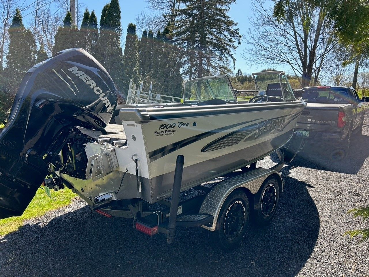 Boat on a trailer, with a black outboard motor, parked outdoors in front of a truck.