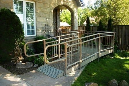 Exterior of a house with a metal wheelchair ramp leading to the entrance, with railings and a textured surface.