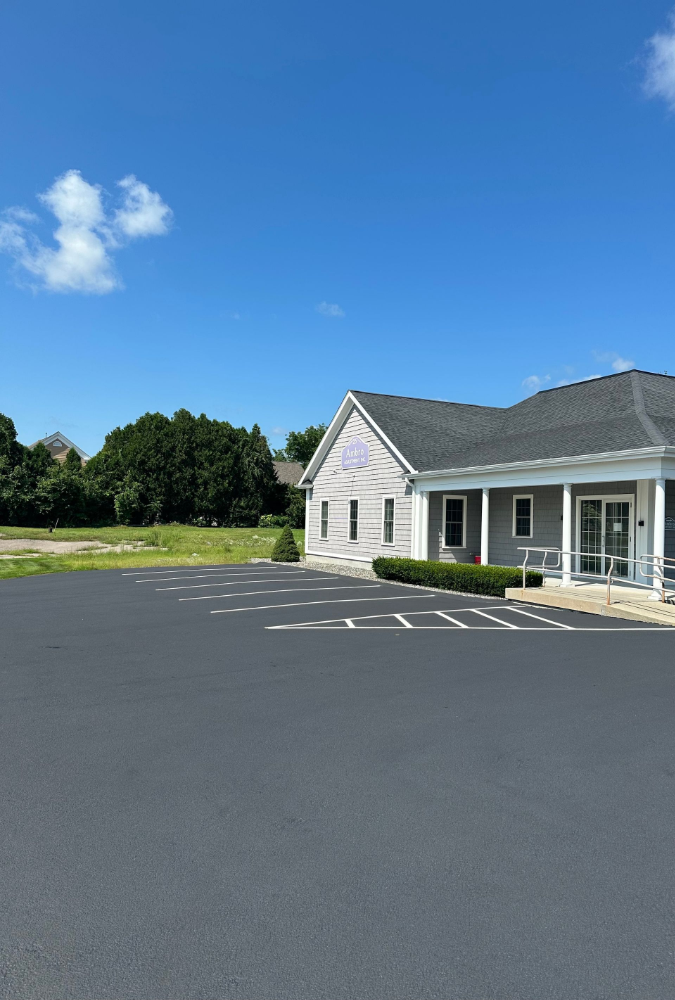 A small white house with a porch and a parking lot in front of it.