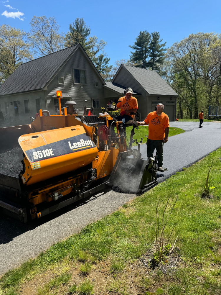 A group of men are paving a driveway in front of a house.