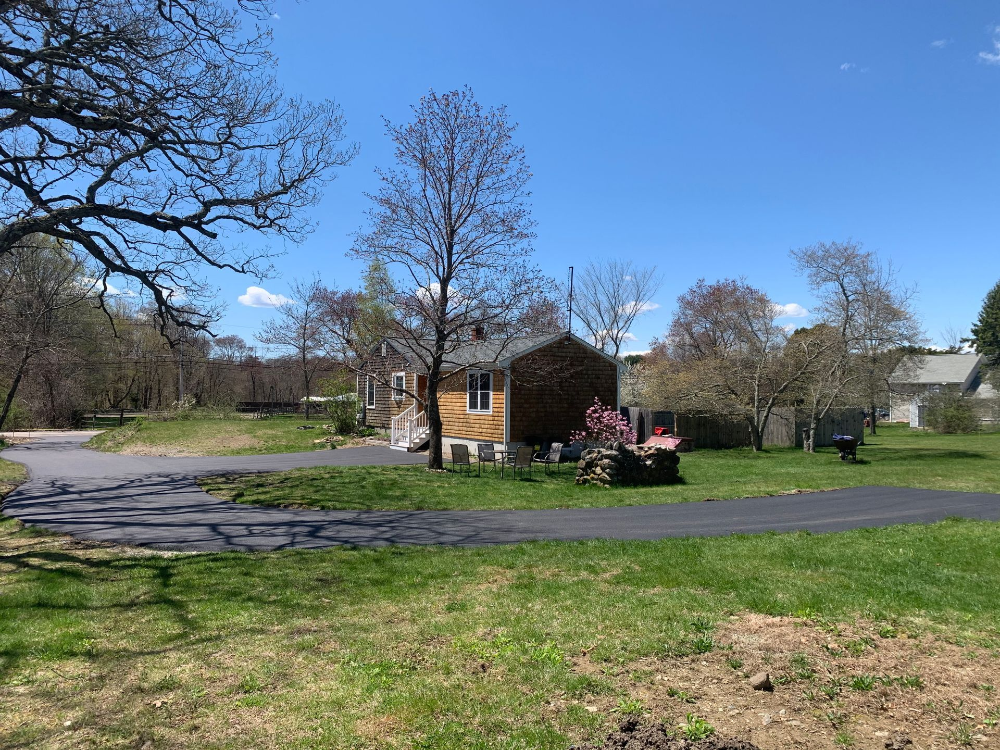A small house is sitting in the middle of a grassy field next to a road.