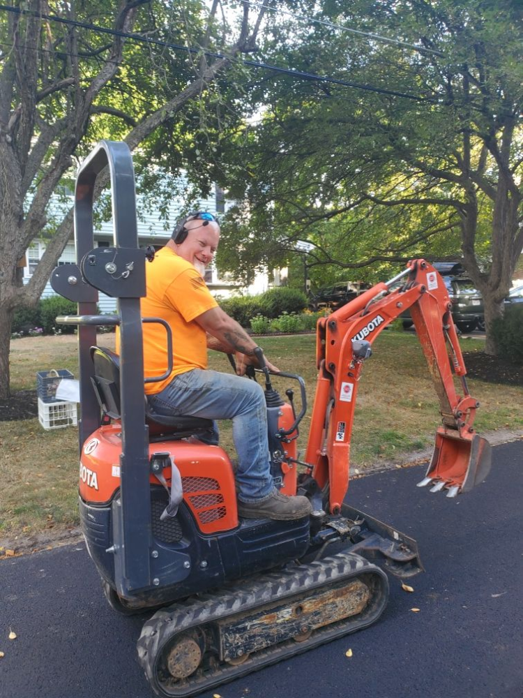 A man in a yellow shirt is sitting on a small orange excavator.