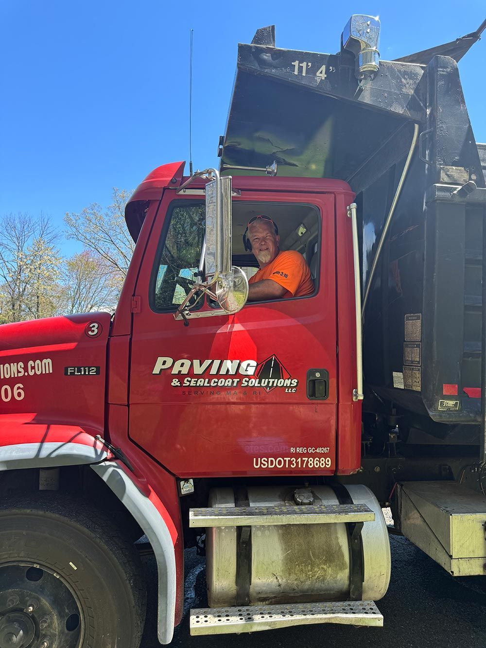 A man is sitting in the driver 's seat of a red dump truck.