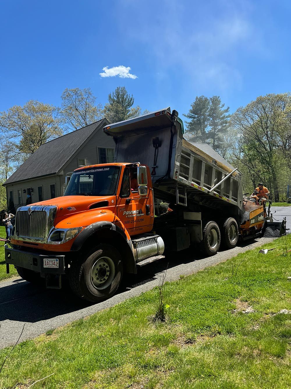 An orange dump truck is parked on the side of a road next to a house.