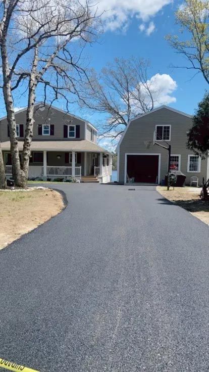 A driveway leading to a house with a barn in the background.