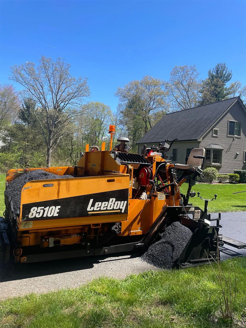 A yellow asphalt paving machine is sitting in front of a house.