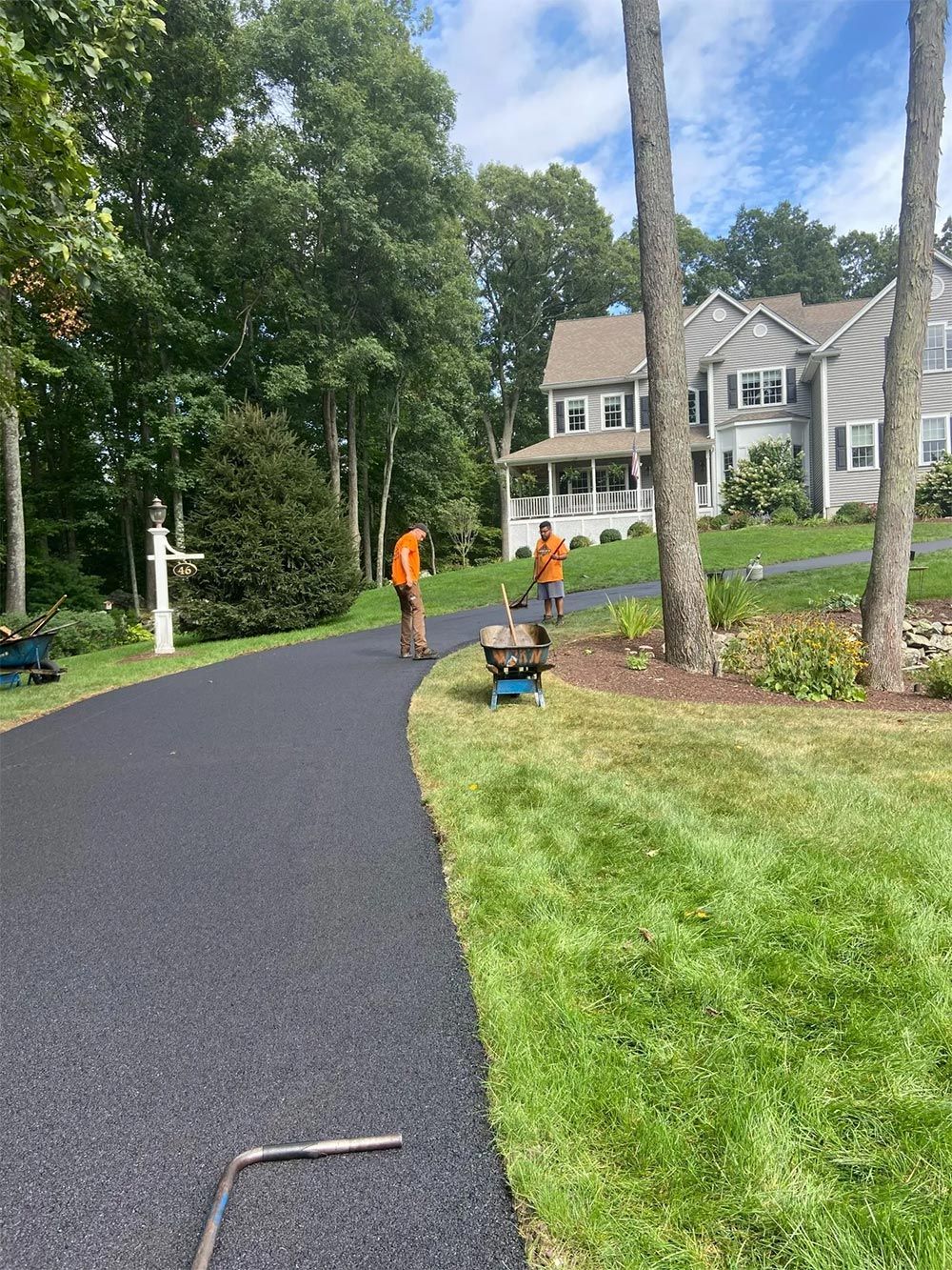 Two men are working on a driveway in front of a house.
