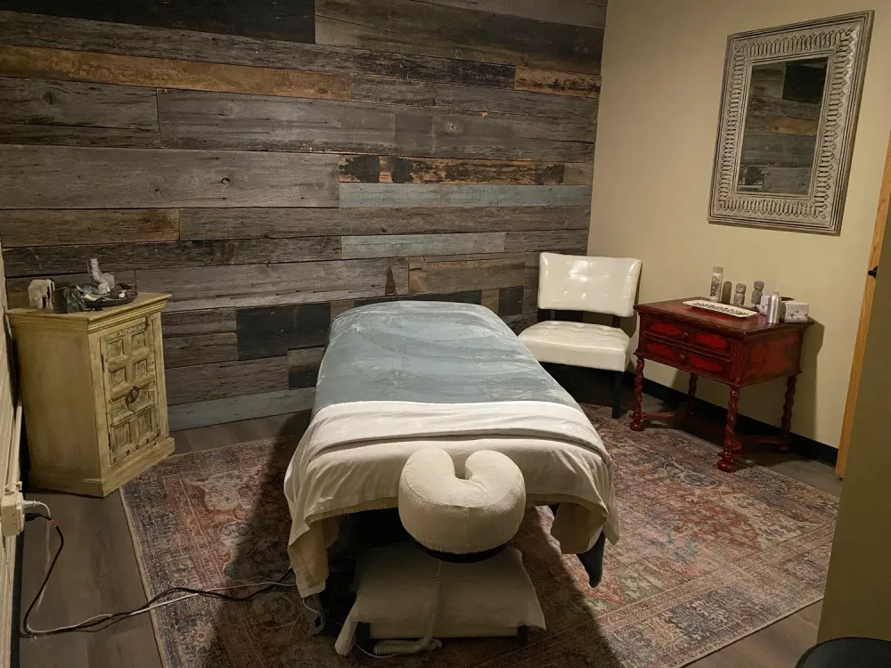 Massage room with treatment table, chair, side table, and wood plank wall decor