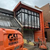 Construction site with orange lift, large windows, and building facade covered in plastic.