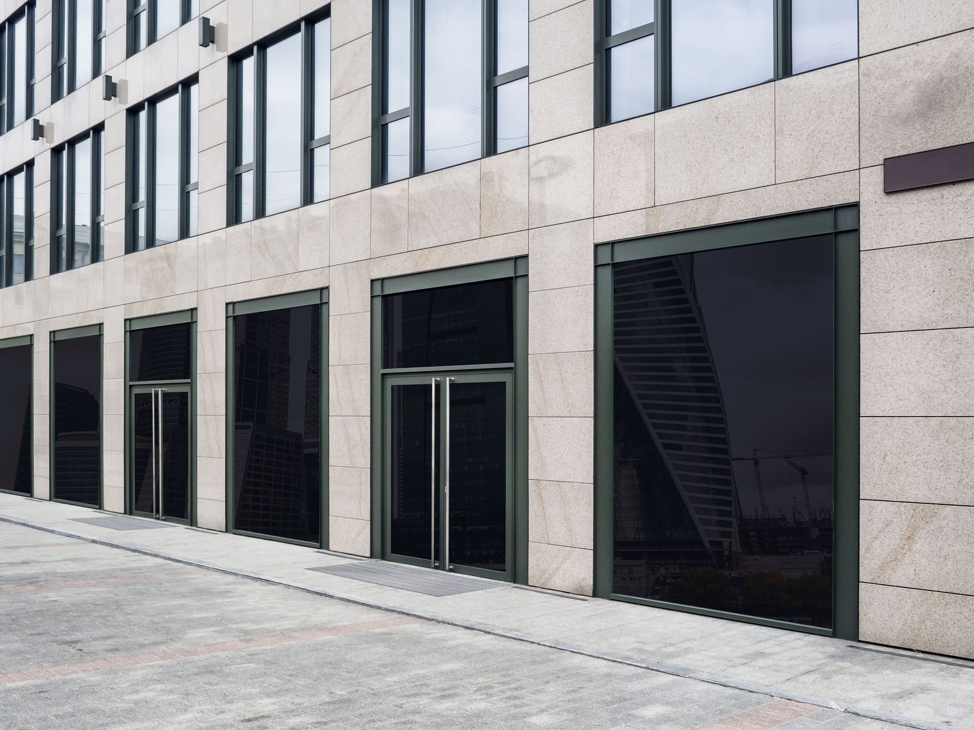Exterior of a modern building with dark-tinted glass storefronts and light-colored stone facade.