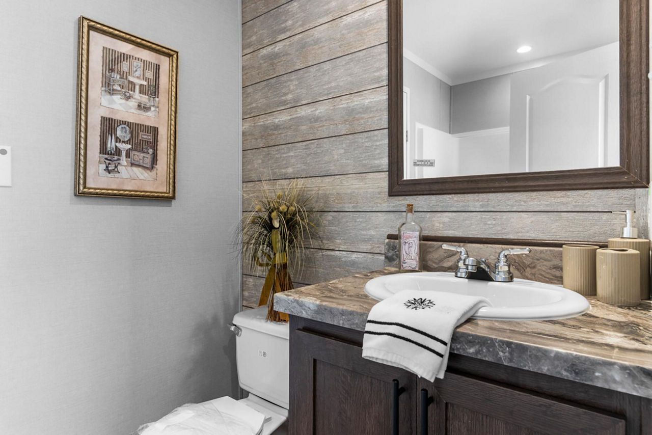 Bathroom with a vanity, mirror, and toilet. Gray and brown color scheme, with a framed picture on the wall.