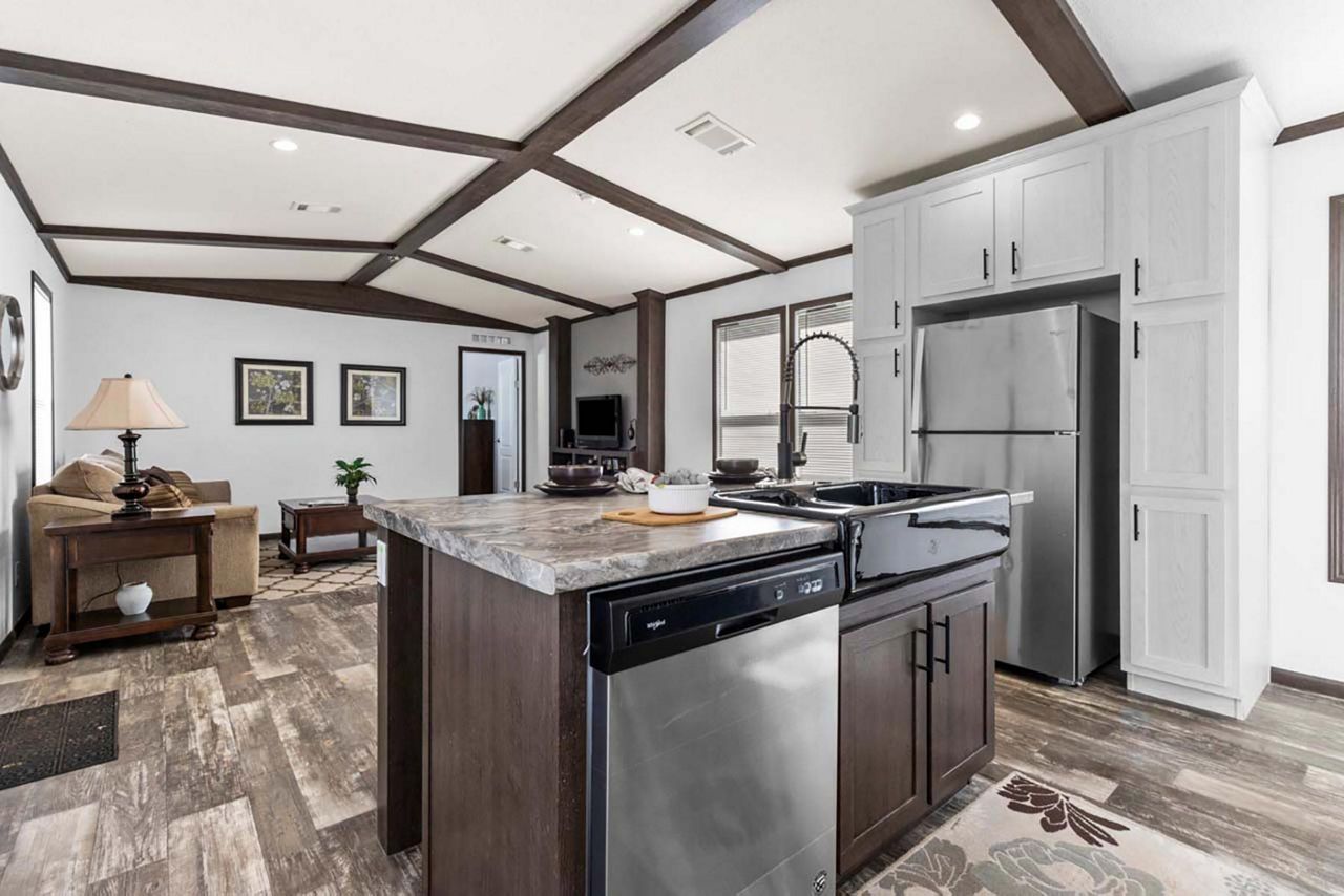 Interior of a modern kitchen with an island and open layout to the living room, featuring stainless steel appliances and dark wood accents.