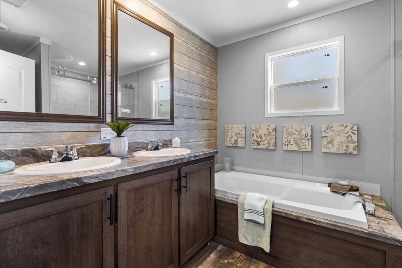Bathroom with double vanity, bathtub, and gray walls. Dark brown cabinetry, large mirrors, and decorative art.