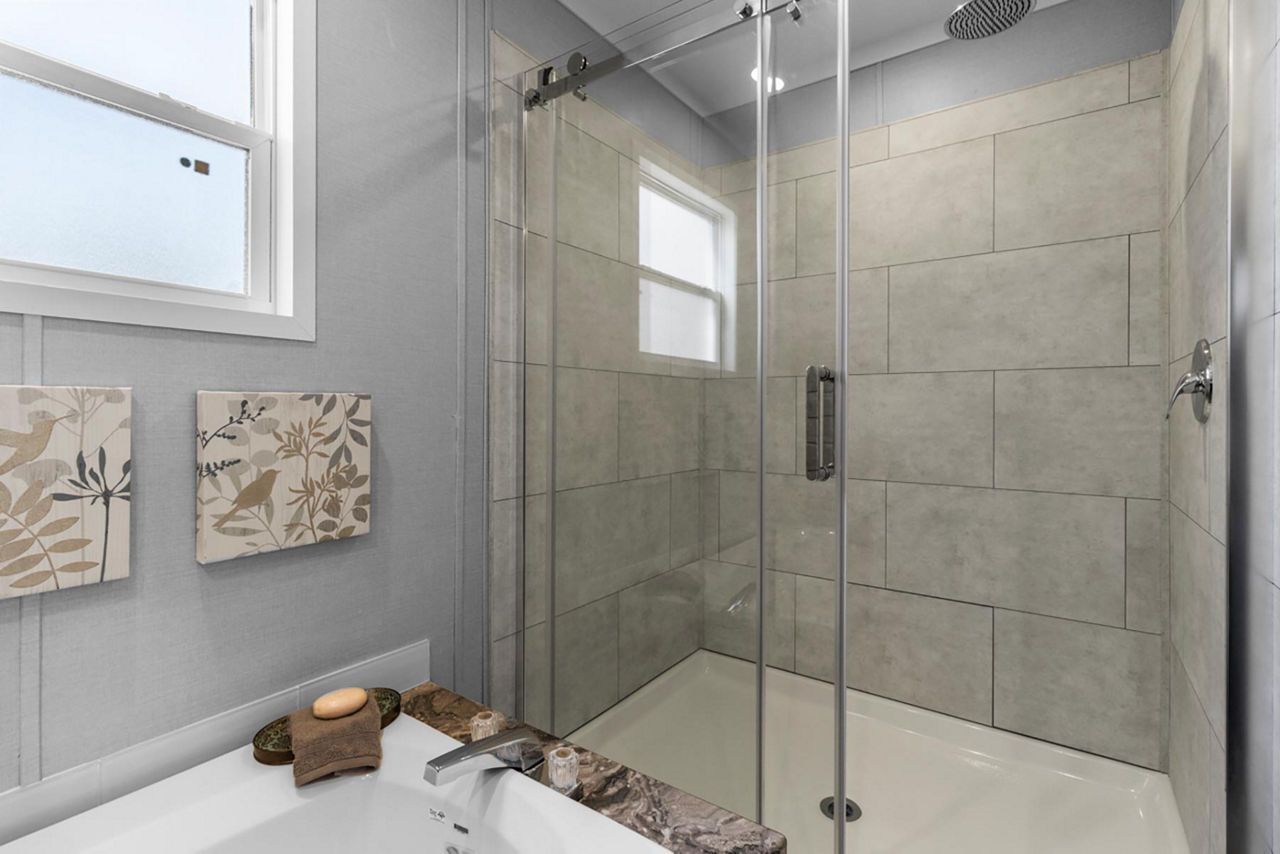 Bathroom with glass shower, tiled walls, and a window. Soft gray color scheme with natural decor.