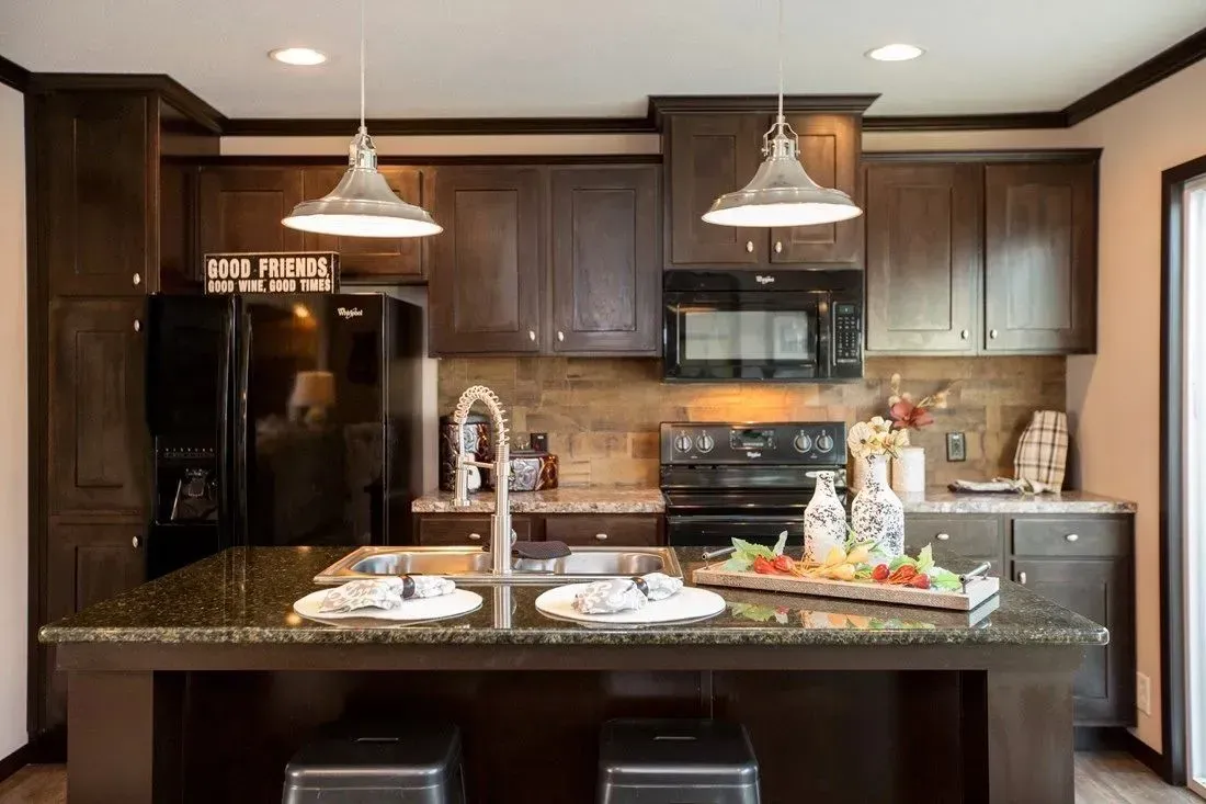A kitchen with a large island , stove , refrigerator , sink , and microwave.