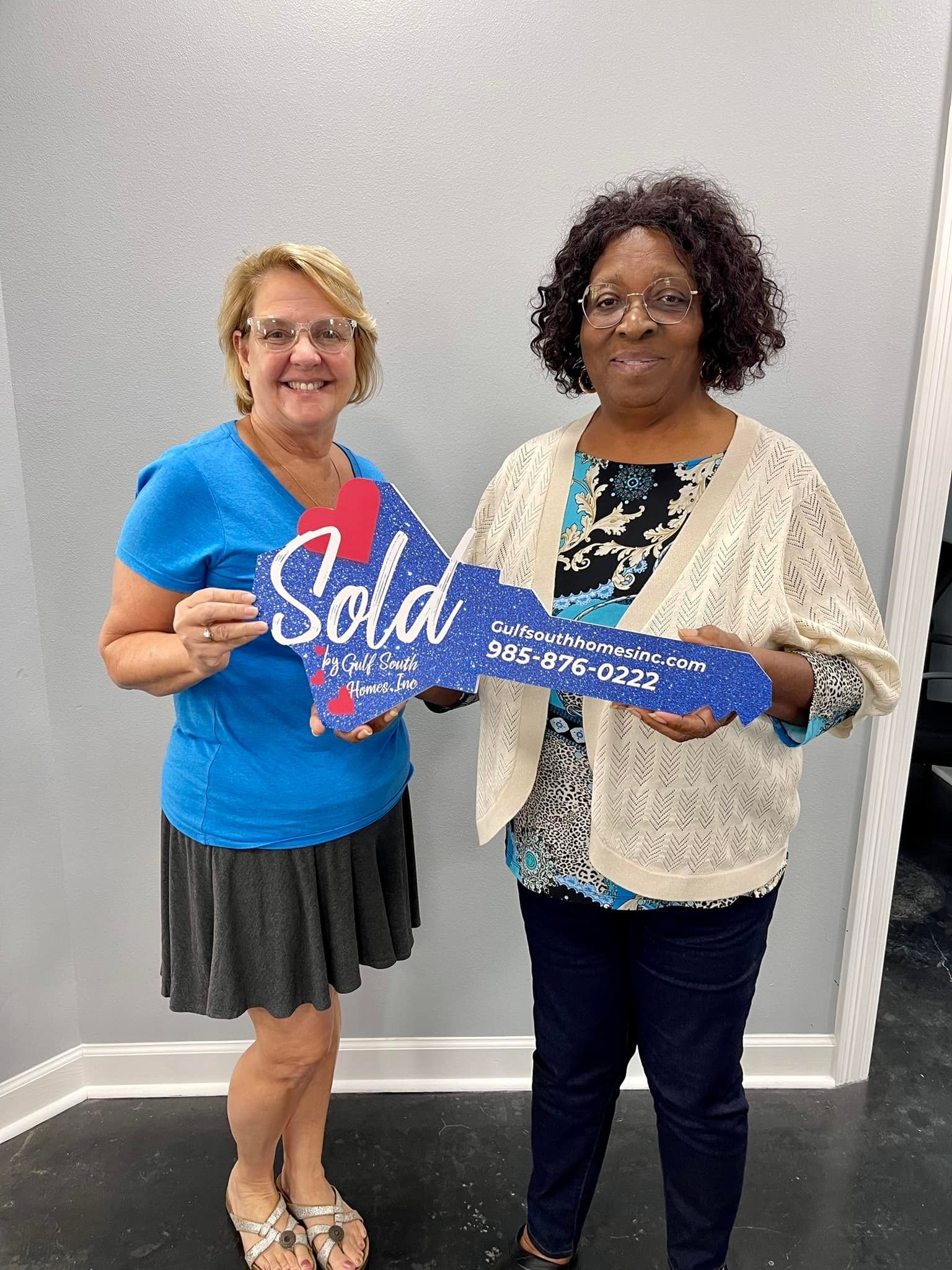 Two women are standing next to each other holding a sold sign.