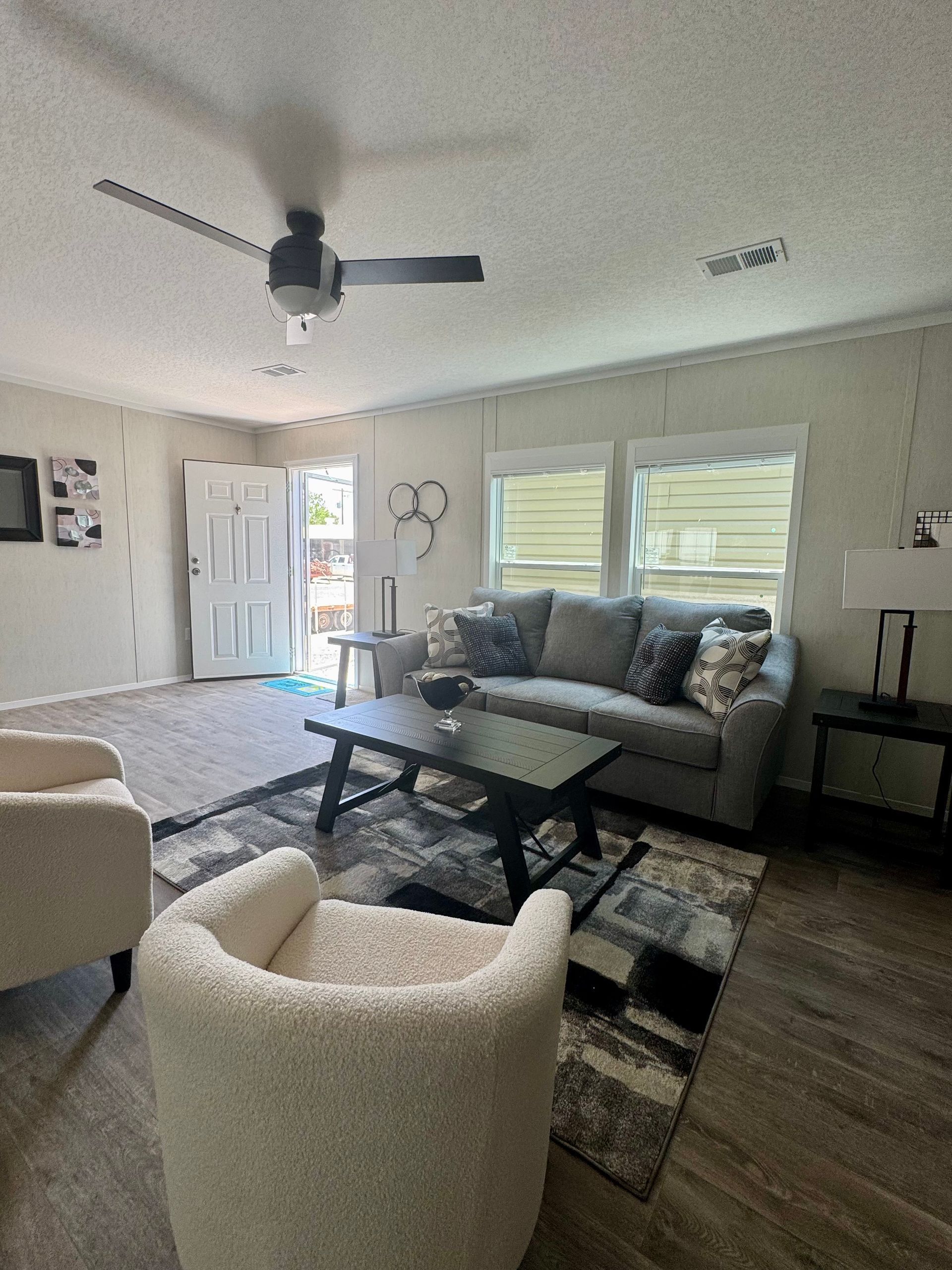 A living room with a couch, chairs, a coffee table, and a ceiling fan.