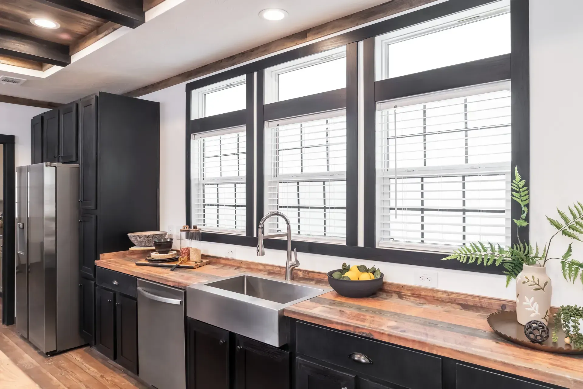 A kitchen with black cabinets, stainless steel appliances, a sink, and a refrigerator.