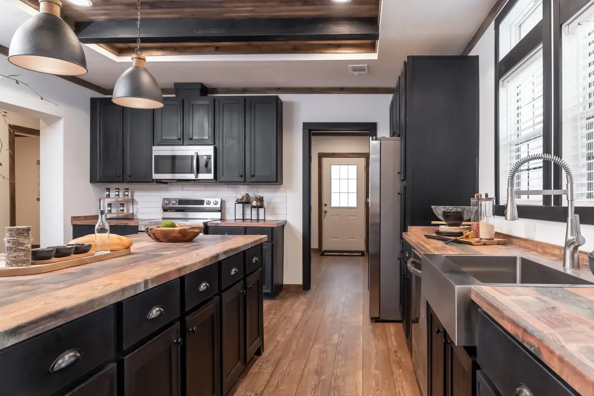 A kitchen with black cabinets, wooden counter tops, stainless steel appliances, and a sink.