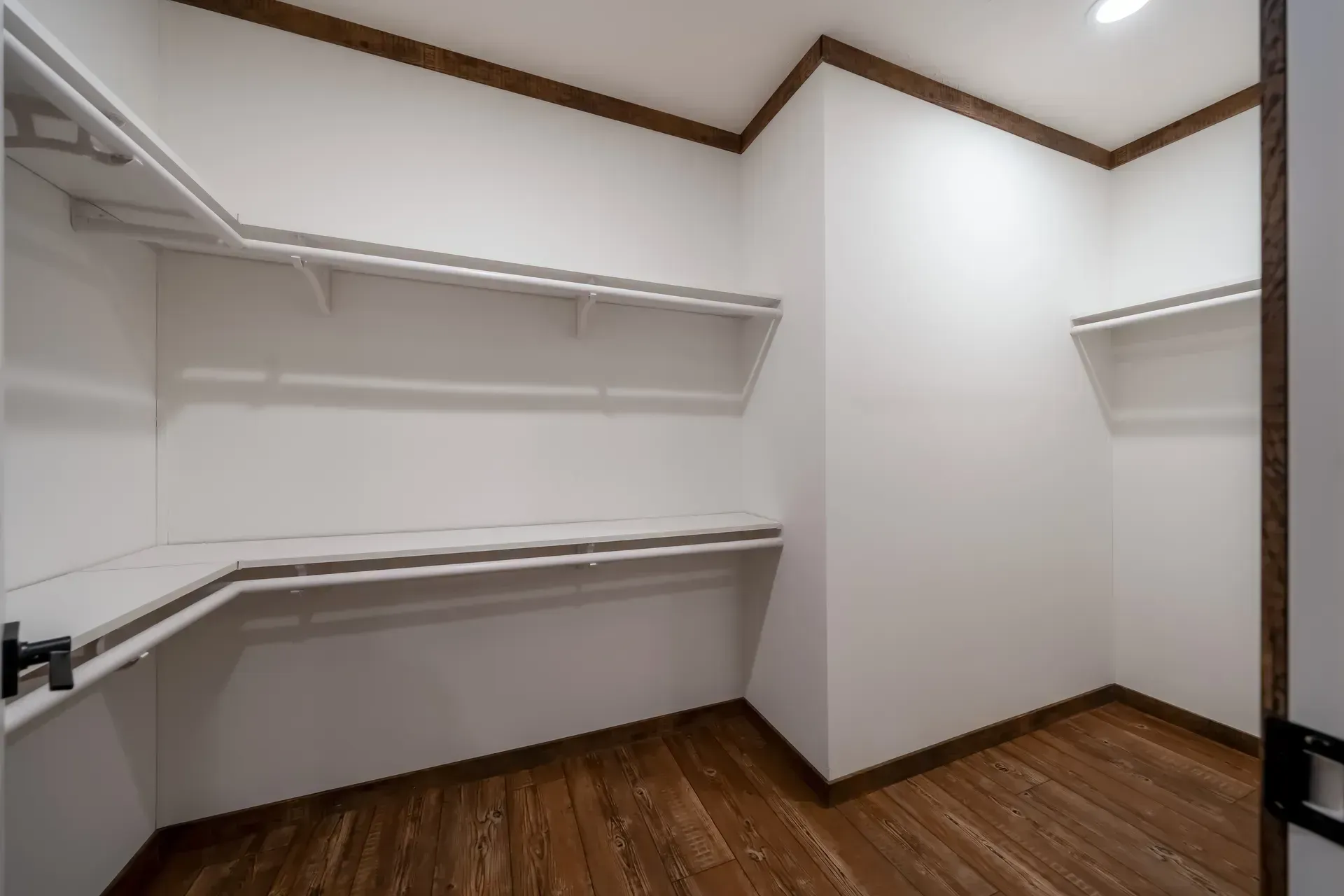 An empty walk in closet with wooden floors and white shelves.