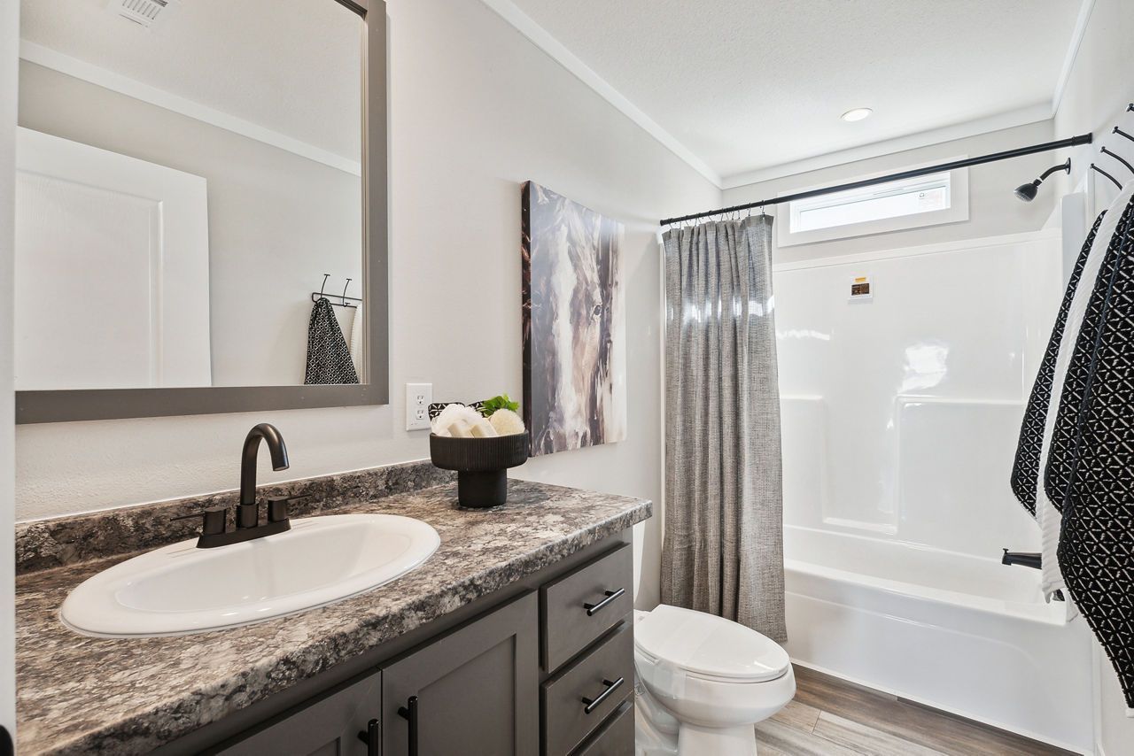 Bathroom with gray cabinets, white sink and toilet, shower with gray curtain, and artwork.