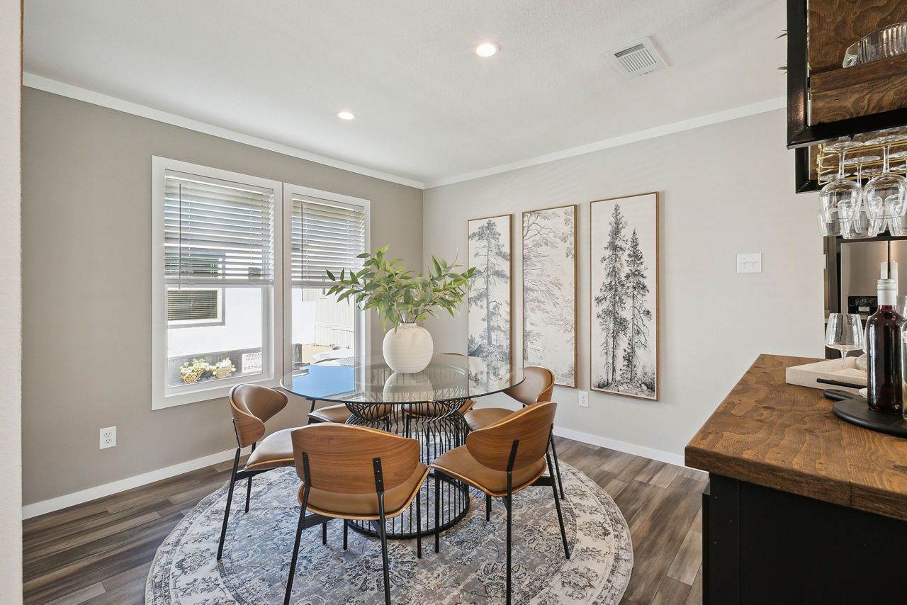 Dining room with a glass-topped table, four chairs, and artwork; neutral walls and a rug.