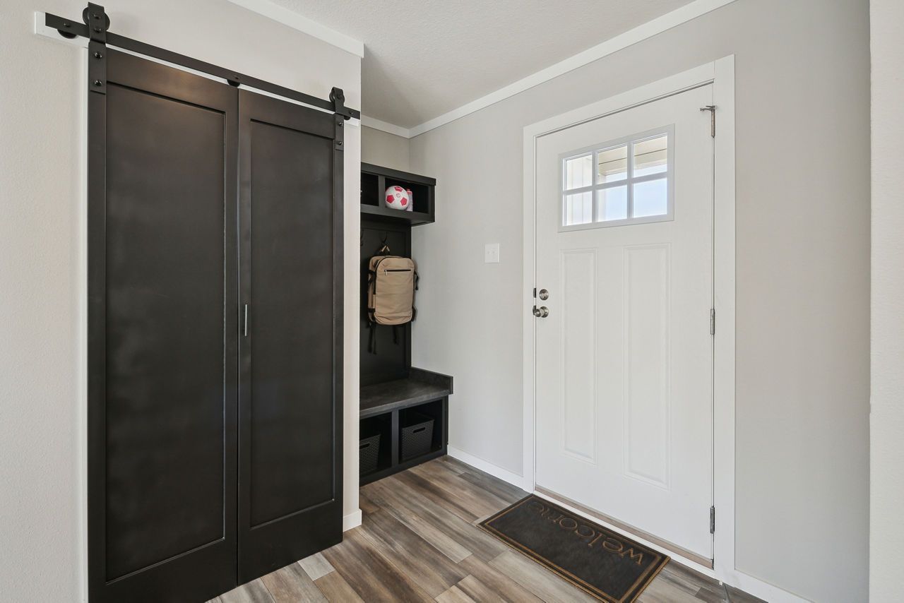 Entryway with black sliding barn door, white door, bench, and gray walls.
