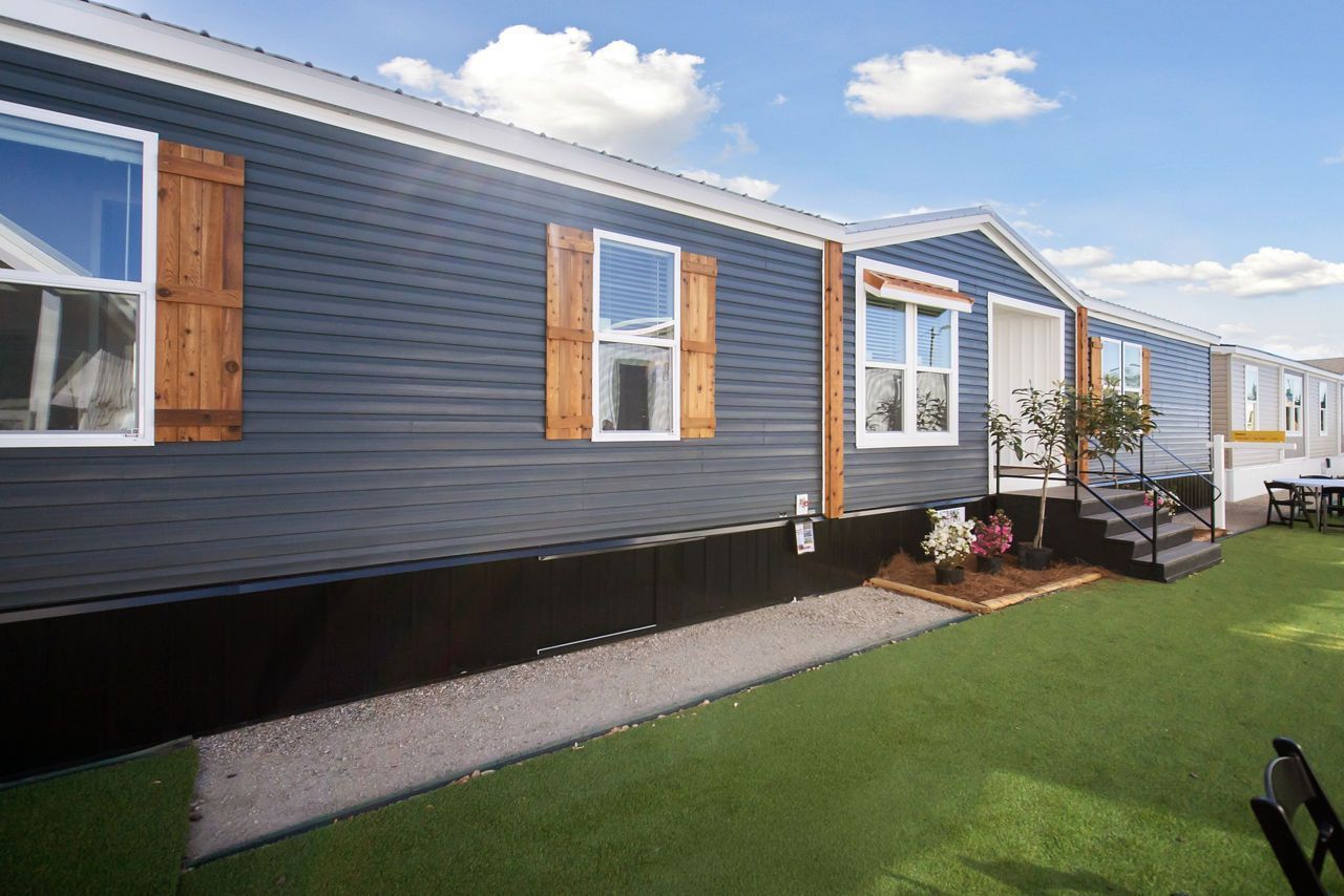 Blue mobile home with brown shutters and a small porch on a green lawn.