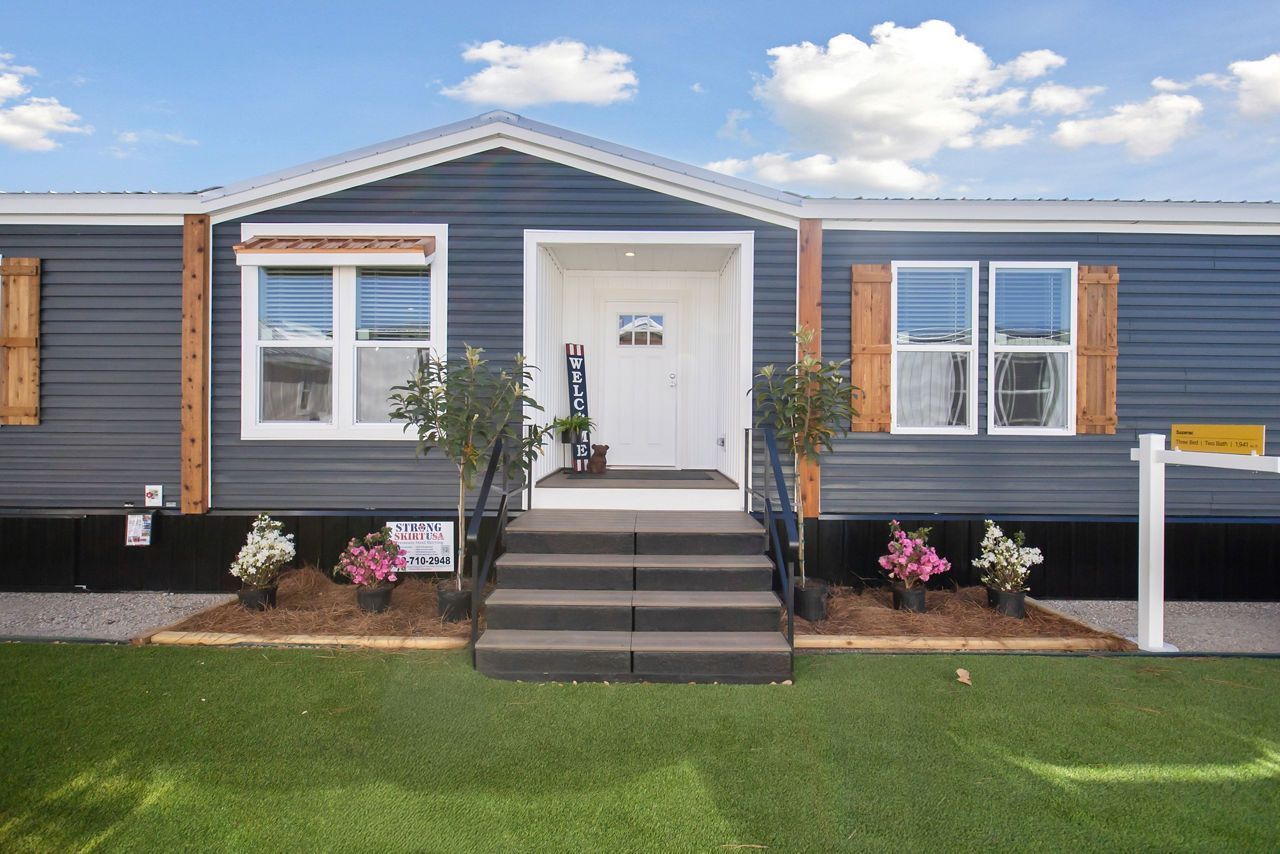 Blue house with white door, steps, and flower beds in front of artificial turf.