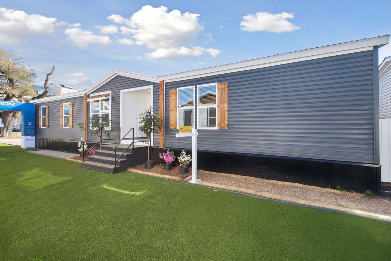 Blue-sided single-story home with white trim, brown shutters, and a small front yard with grass.