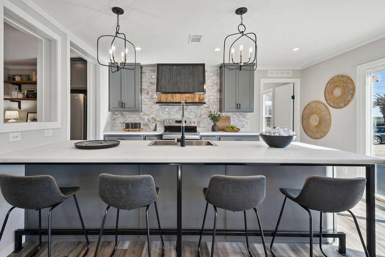 Modern kitchen with gray island, cabinets, and bar stools. Bright light and decor.