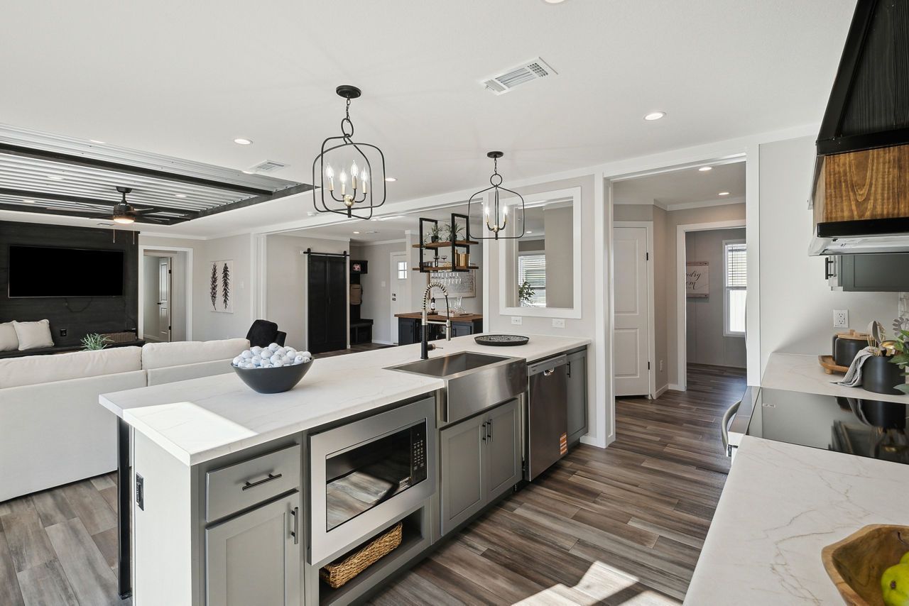 Modern kitchen with stainless steel island, white countertops, and wooden floors.