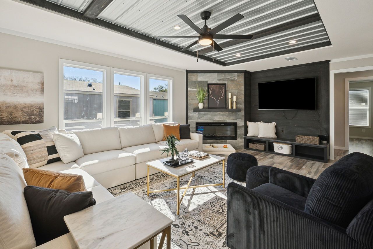 Spacious living room with white sectional, fireplace, large windows, dark accent wall, and patterned rug.