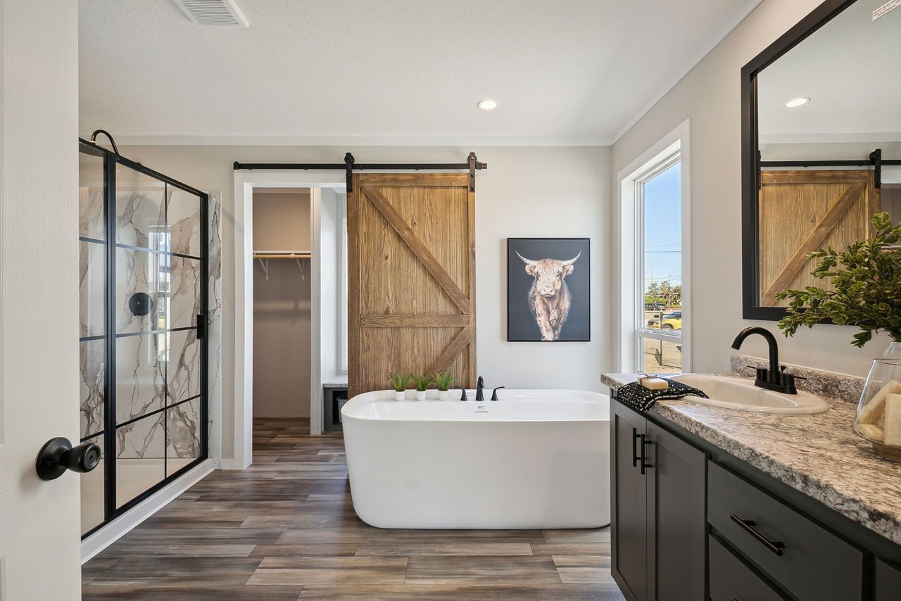 Modern bathroom with freestanding tub, barn door, black vanity, and walk-in shower.