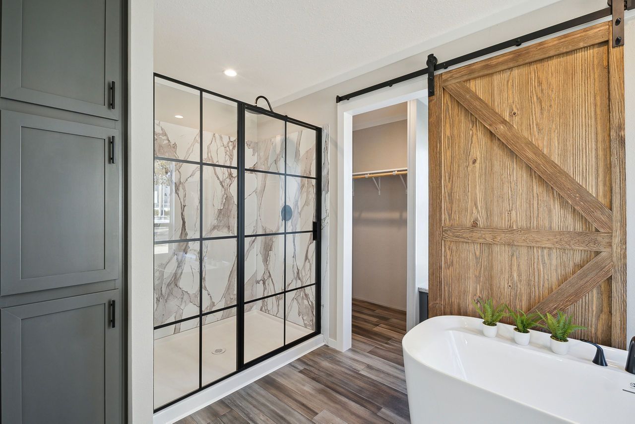 Bathroom with glass shower, wooden sliding door, and white bathtub.