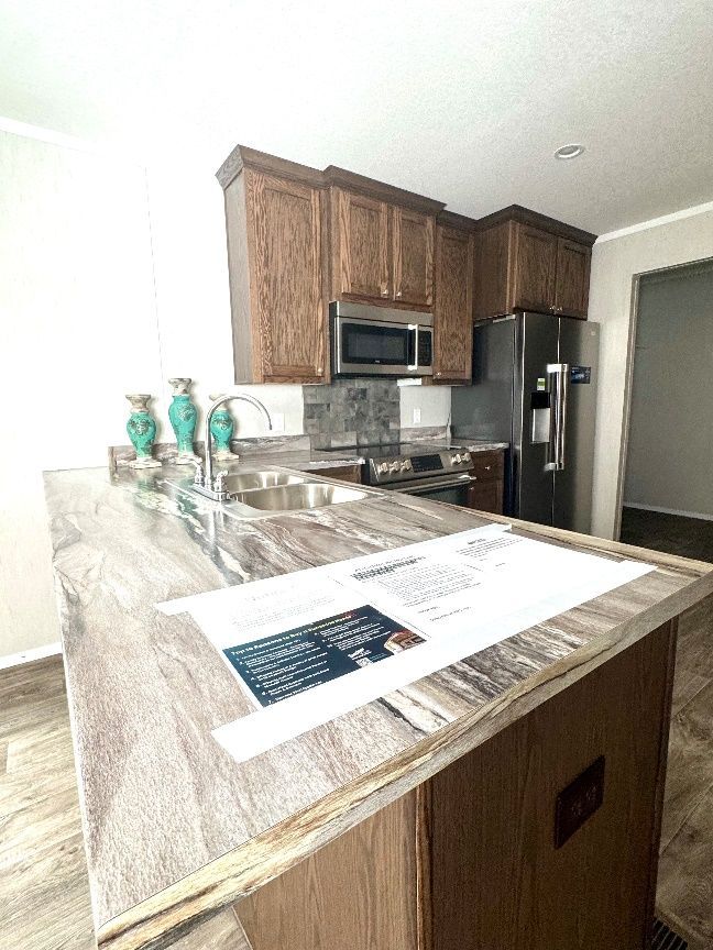 Kitchen with wooden cabinets, stainless steel appliances, and a gray and white countertop island. The setting appears to be a modern home.
