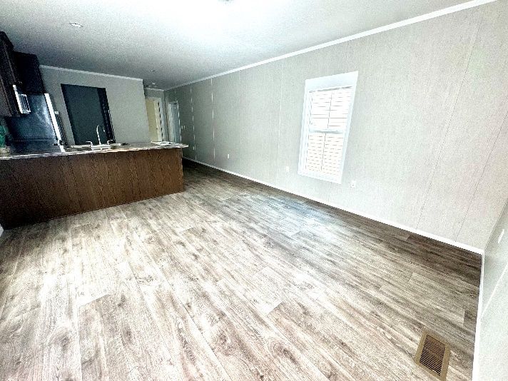 Empty, light-filled room with wooden floor and kitchen island. Light gray walls and neutral-toned flooring.