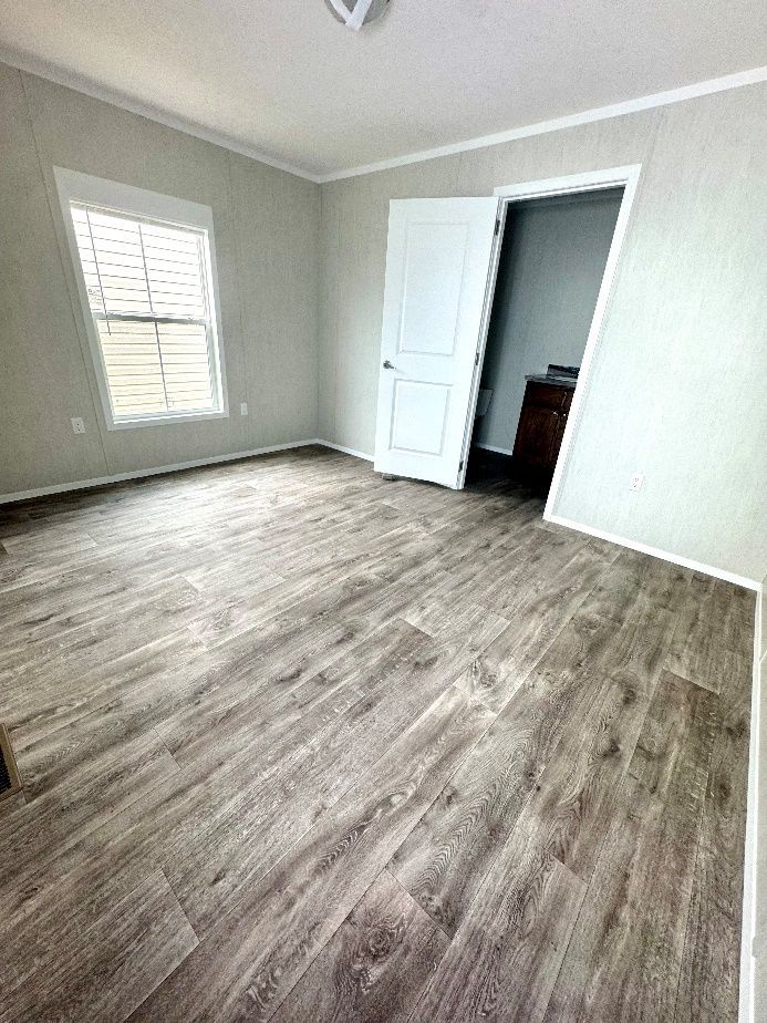 Empty bedroom with wood-look flooring, a window with blinds, and a white door leading to another room.