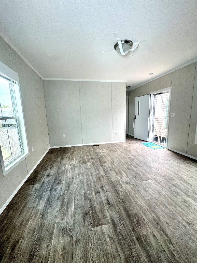 Empty room with laminate flooring, white walls, and a ceiling light. A window and a door are visible.