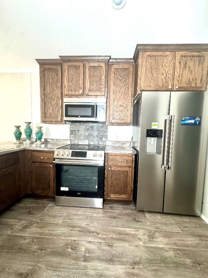 A kitchen with wooden cabinets, stainless steel appliances, and a light-colored countertop.  A side-by-side refrigerator and stove are visible.