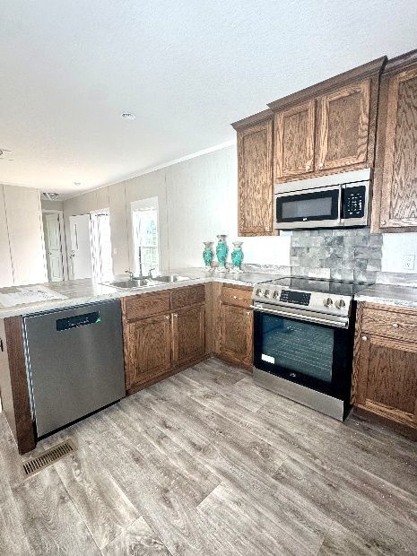 Kitchen with wooden cabinets, stainless steel appliances, and light wood-look flooring. A sink and dishwasher are visible, along with a stove.