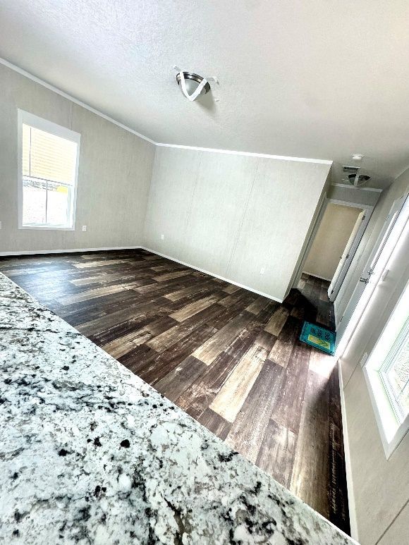 Interior of a room with dark wood-look flooring and a white wall. A granite countertop is in the foreground.